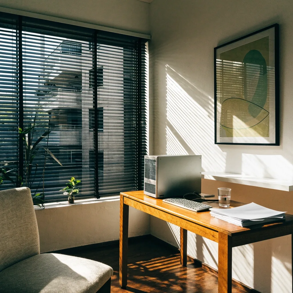 A home office at midday with a humidifier misting beside a keyboard and a chair pushed back from the desk